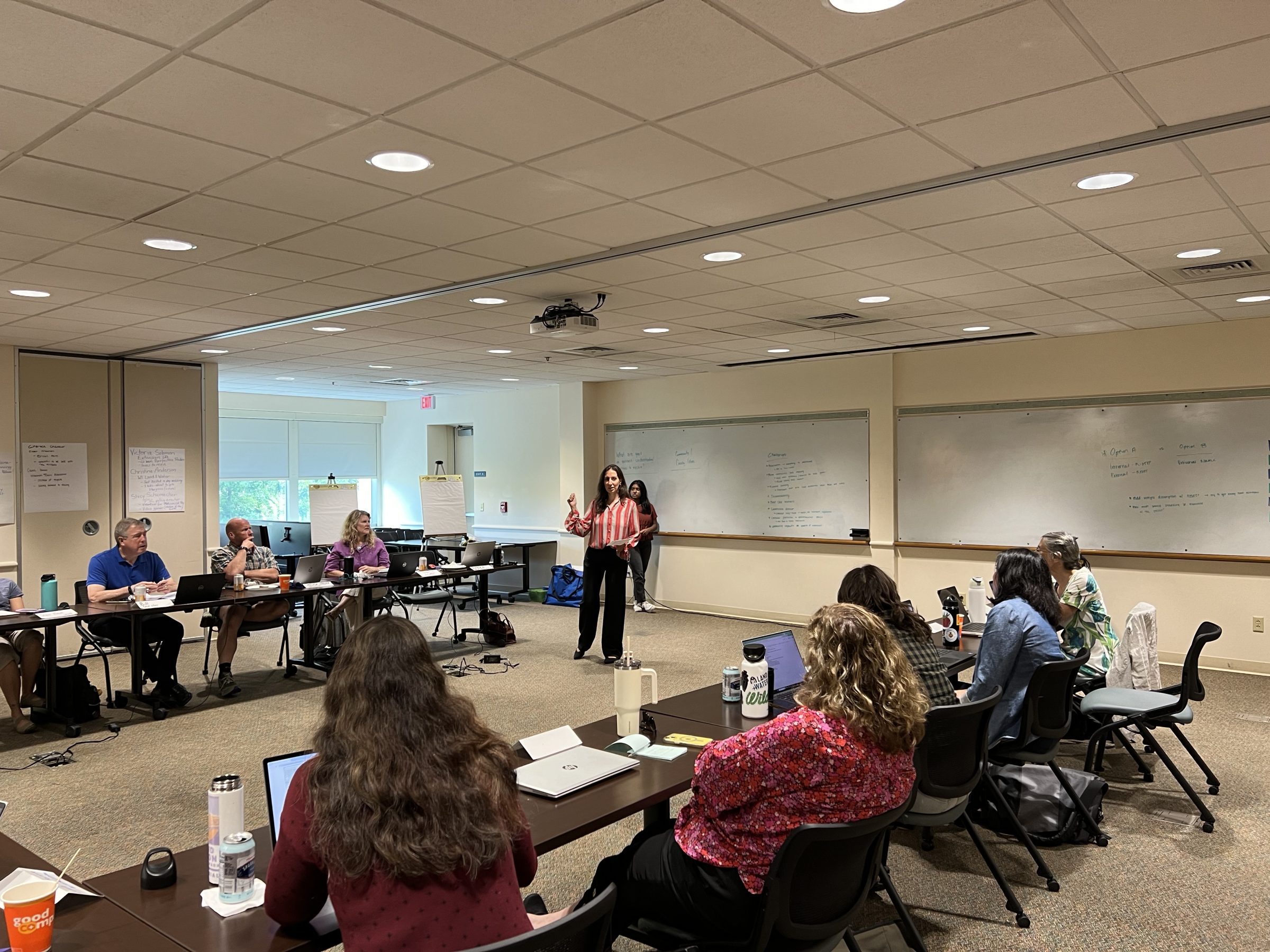Group of community members sitting in a room listening to a woman present. 